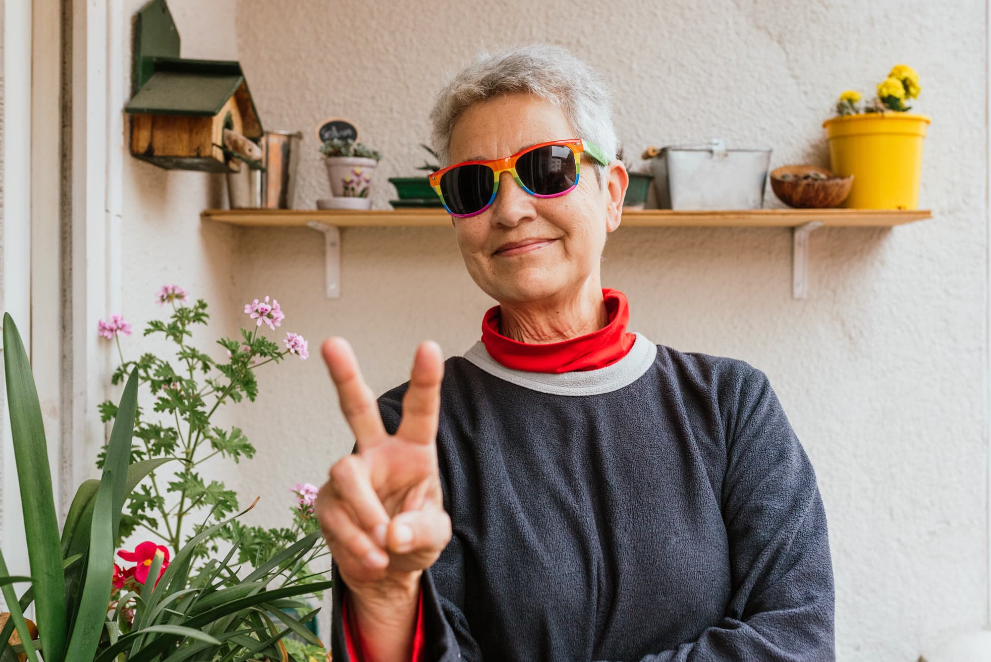 A joyful older adult with rainbow sunglasses giving a peace sign